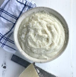 Cheesy mashed cauliflower in a white bowl next to a blue and white kitchen towel.