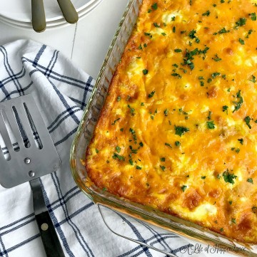 The make ahead breakfast egg casserole in a clear glass baking dish on a blue and white kitchen towel.
