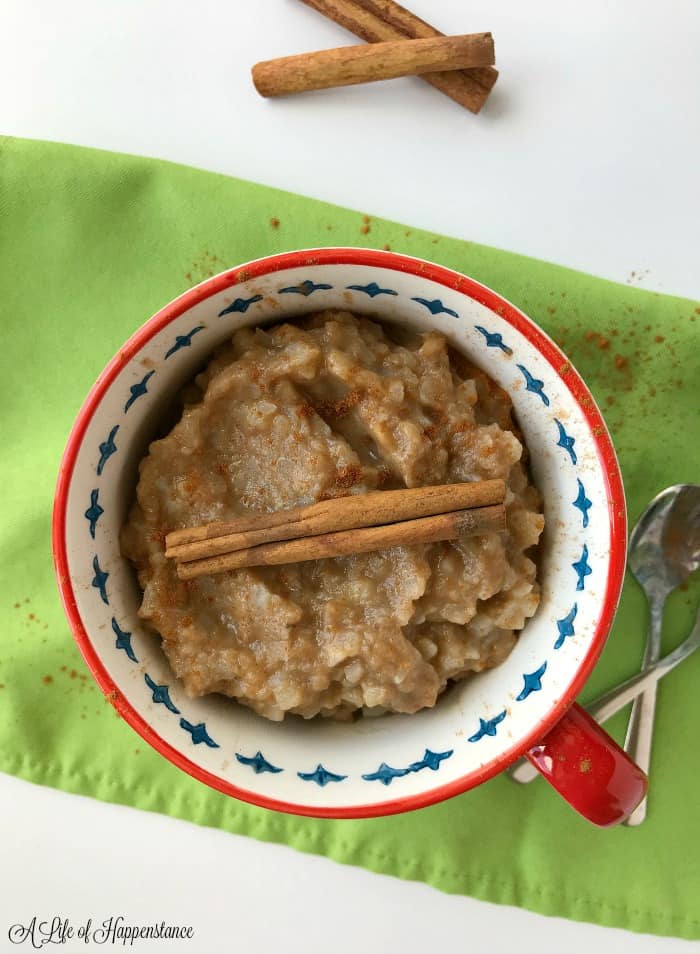 A bowl of cauliflower rice oatmeal garnished with a cinnamon stick sitting on a green napkin. 