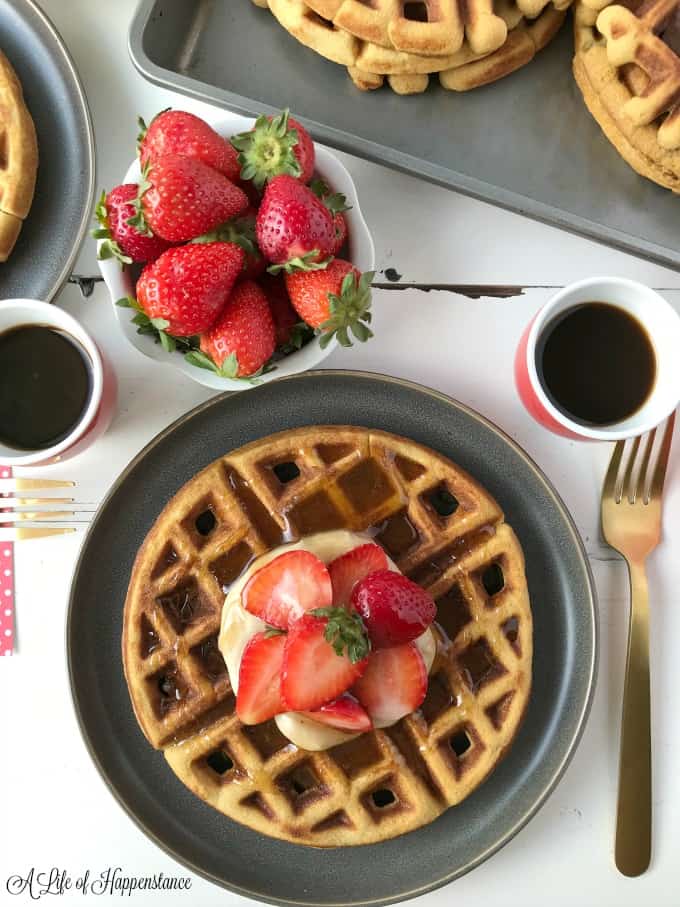 Waffles in a baking tray. One waffle on a grey plate topped with cashew cream, strawberries and cinnamon honey syrup. 