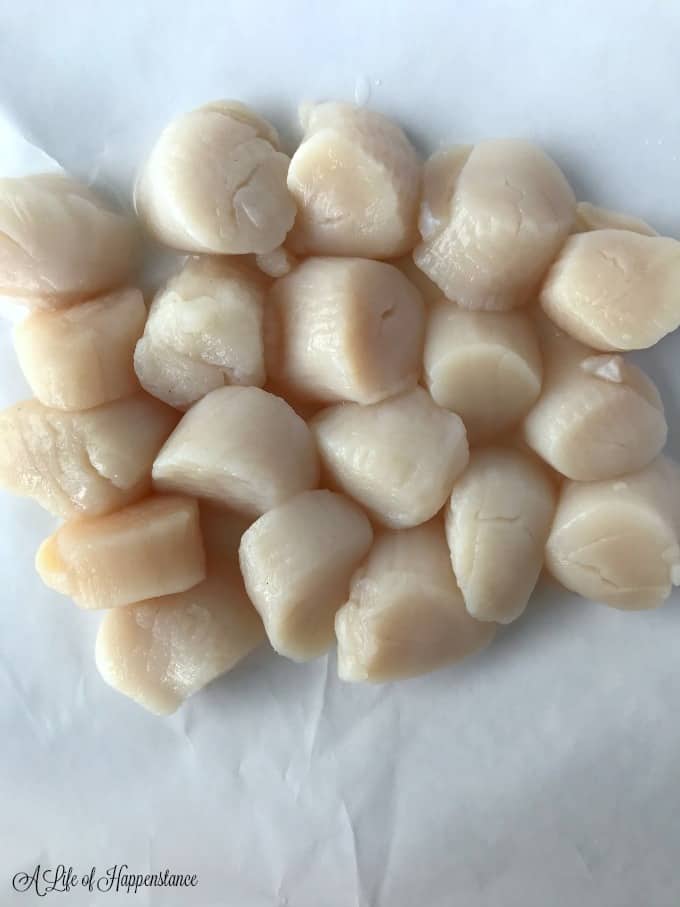 Fresh, uncooked sea scallops on white wax paper.