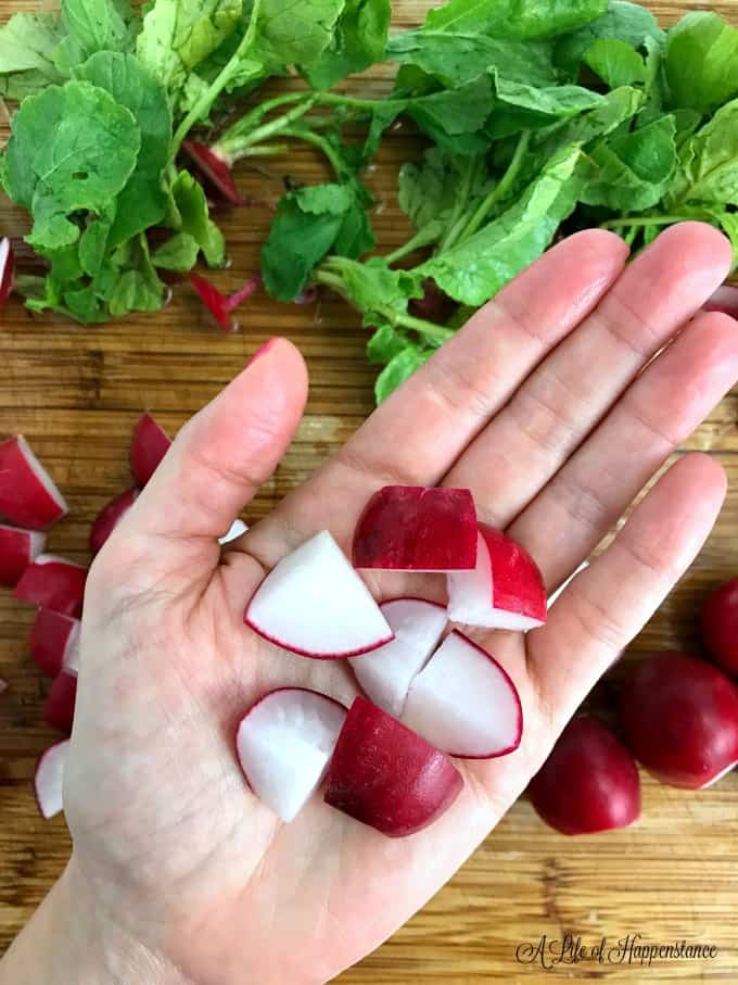 Fresh quartered radishes being held in the palm of a hand. 