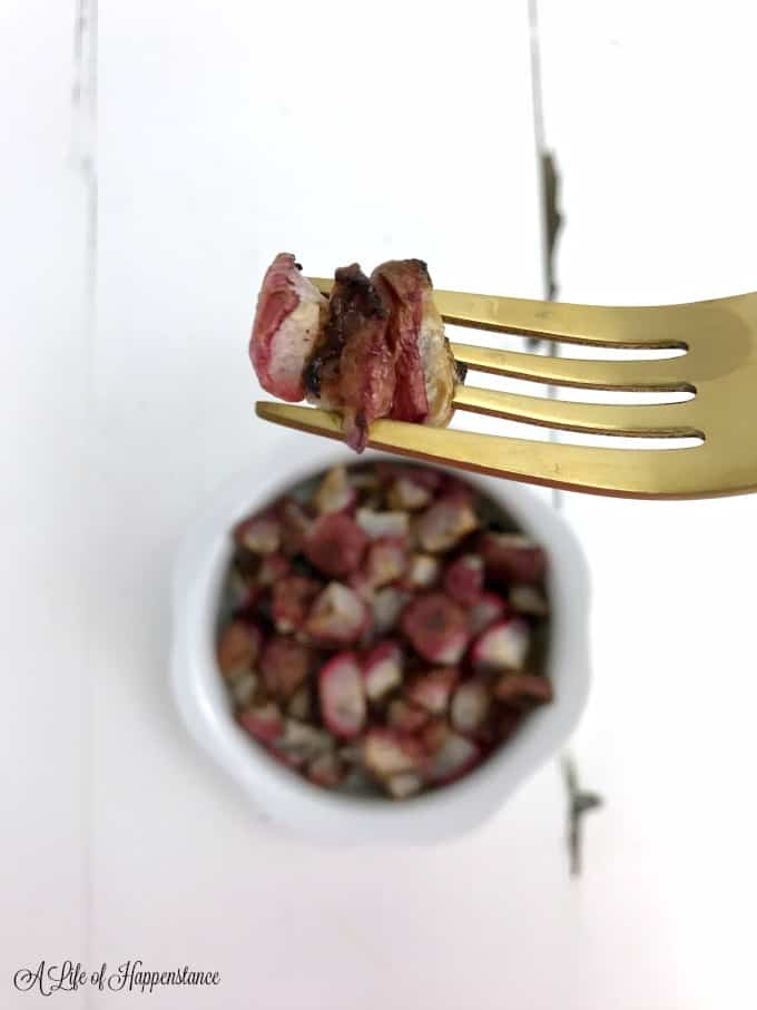 Close up of roasted radishes on a gold fork. The rest of the radishes are in a white bowl in the background. 
