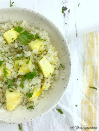 A white bowl filled with coconut cauliflower rice and pineapple.