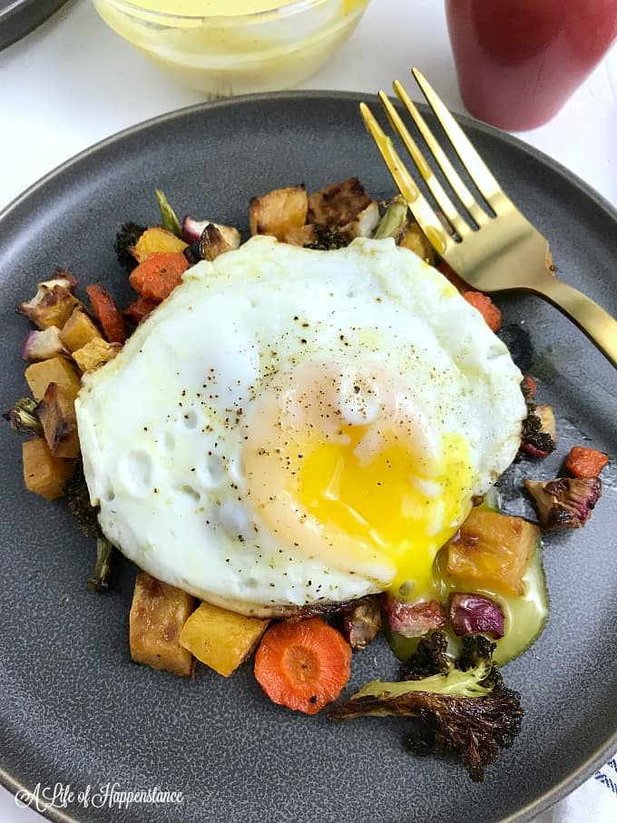A grey plate filled with roasted vegetables and topped with an egg. 