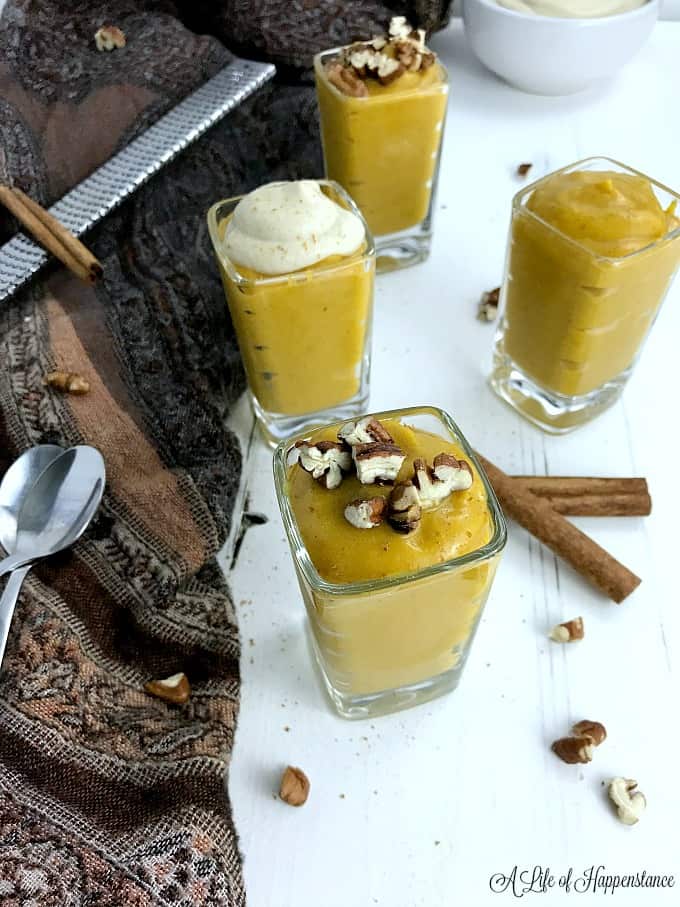 Paleo pumpkin pudding in small glasses topped with chopped nuts and cashew cream. 