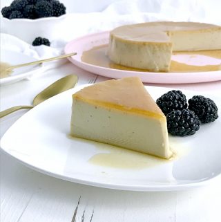 A slice of Cuban flan on a white plate garnished with blackberries.