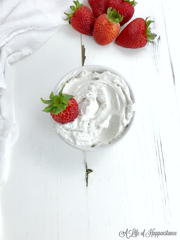 A small white bowl filled with whipped coconut cream and one red strawberry. 