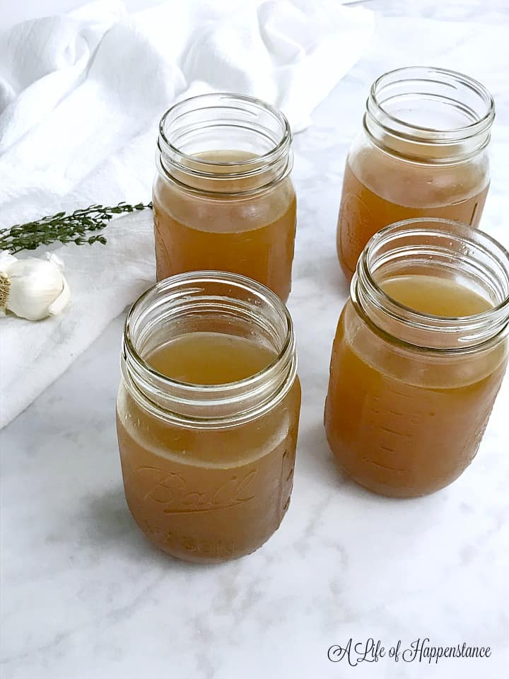Four mason jars filled with homemade vegetable broth sitting on a table. 