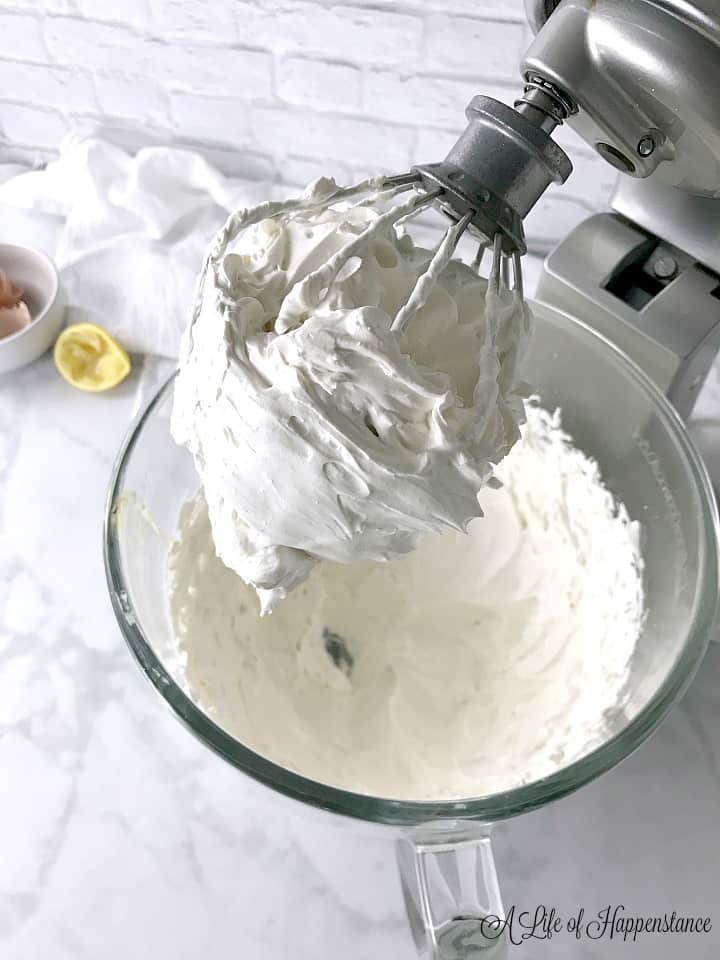 A whisk on the stand mixer filled with the meringue frosting. 