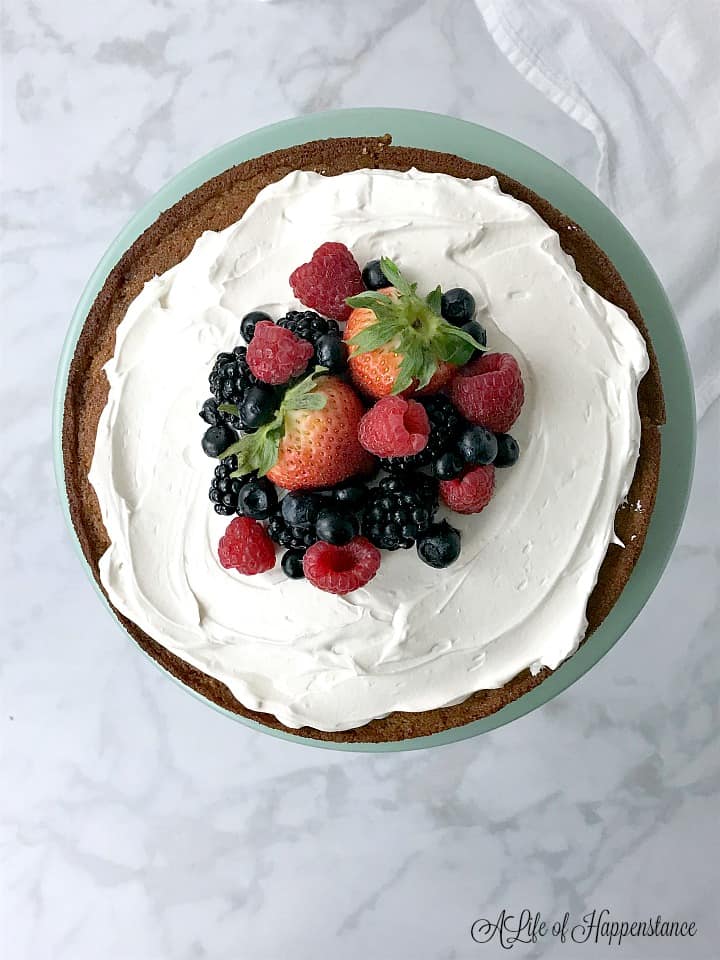 An overhead photo of the vanilla almond flour cake topped with honey Italian meringue and fresh berries. 