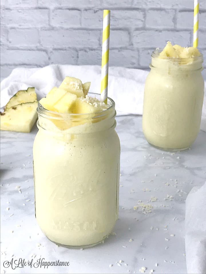 Side shot of two mason jars on a table filled with pineapple coconut smoothie and garnished with pineapple chunks and shredded coconut. 