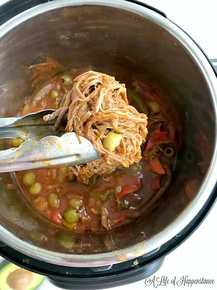 Using tongs to remove the completed Cuban Ropa Vieja recipe from the Instant Pot. 