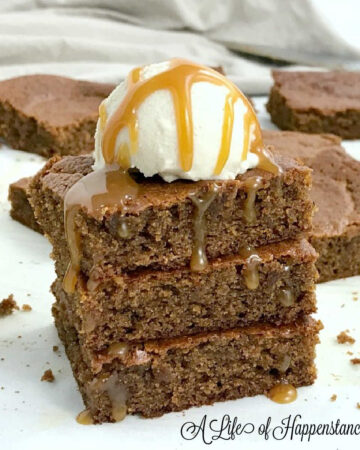 A stack of three pumpkin blondies topped with vanilla ice cream and drizzled with caramel sauce.
