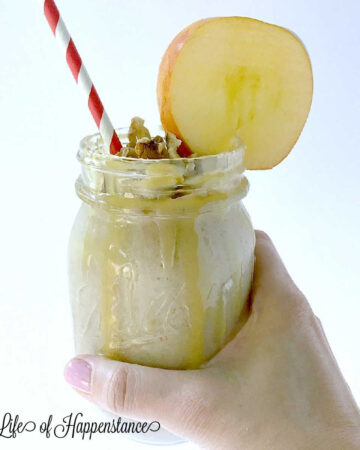 Holding a mason jar filled with an apple cinnamon smoothie, garnished with an apple slice.