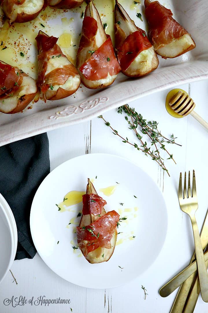 A slice of the cooked prosciutto wrapped pear on a white plate while the rest of the elegant appetizer is in the baking dish. 