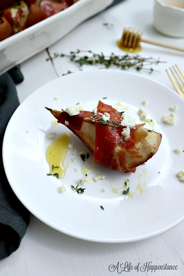 A slice of pear wrapped in prosciutto , sprinkled with fresh thyme, cheese and drizzled with honey on a white plate. 