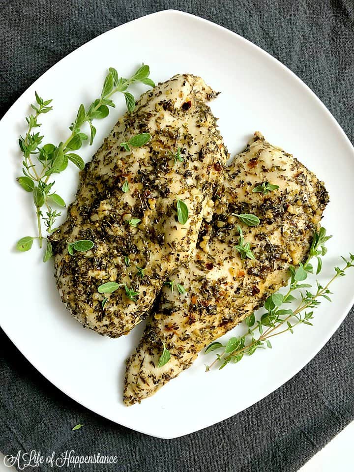 Two pieces of oregano lemon chicken on a white plate with fresh oregano as a garnish. 