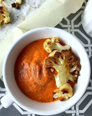A white bowl filled with the roasted cauliflower red pepper soup and garnished with roasted cauliflower florets.