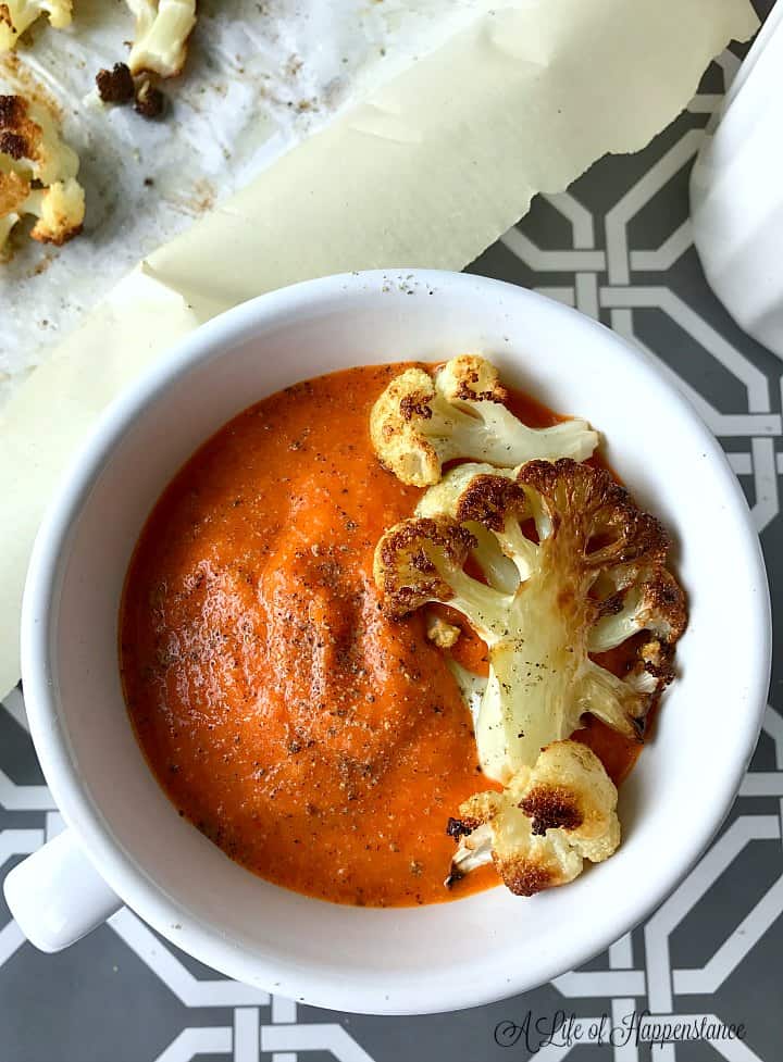 The soup in a white bowl with pieces of roasted cauliflower on top. 