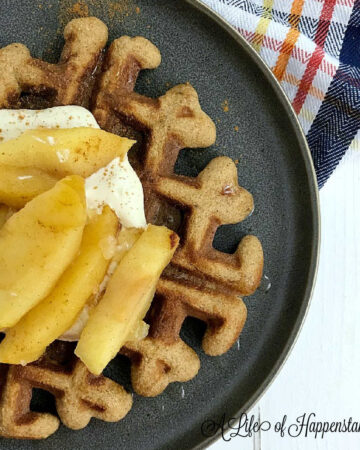 A waffles garnished with cashew cream and apples on a gray plate.