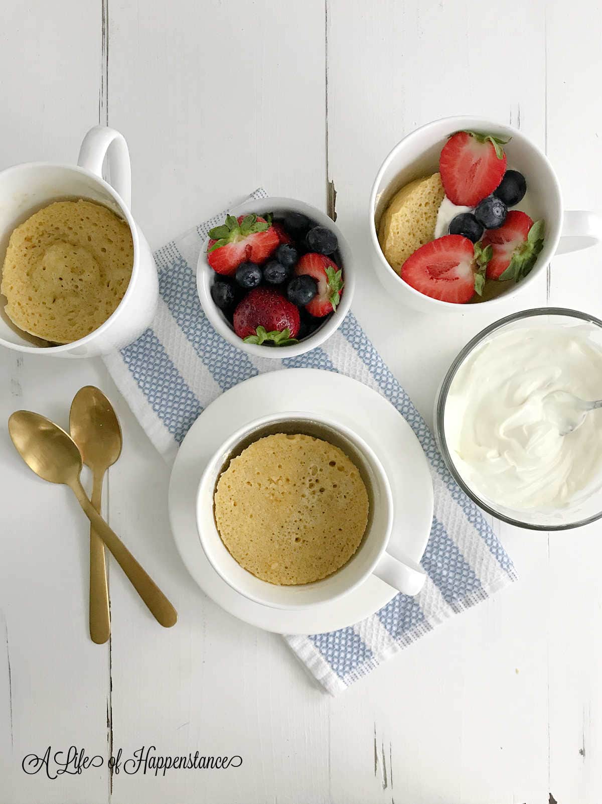 Three fully baked cakes in white mugs with one topped with coconut cream and fresh berries. 
