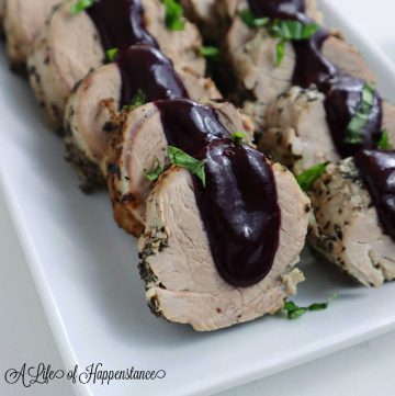 A close up hoto of the berry pork tenderloin with sauce drizzled on top and garnished with fresh basil leaves.