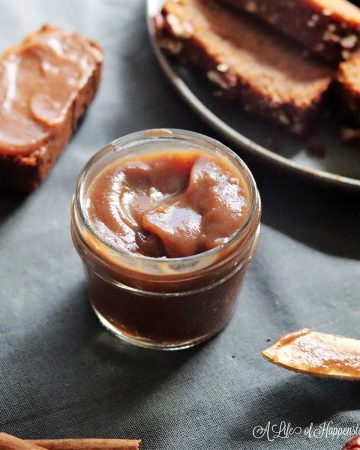Healthy homemade apple butter in a small glass jar surrounded by pumpkin bread.