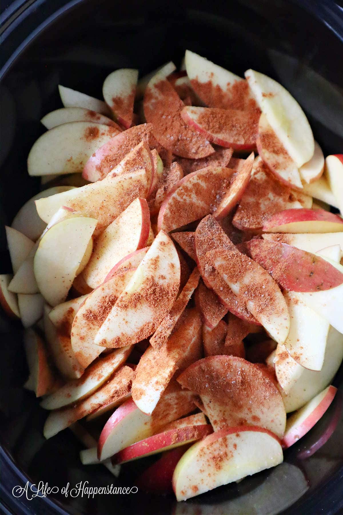 Sliced apples topped with spices in a slow cooker.