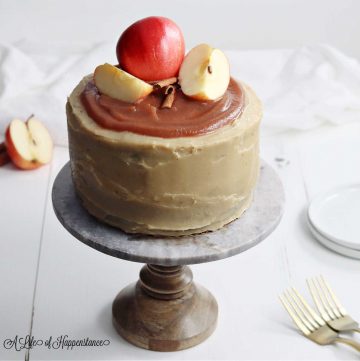 The apple cider layer cake on a cake stand with sliced apples and cinnamon sticks on top.