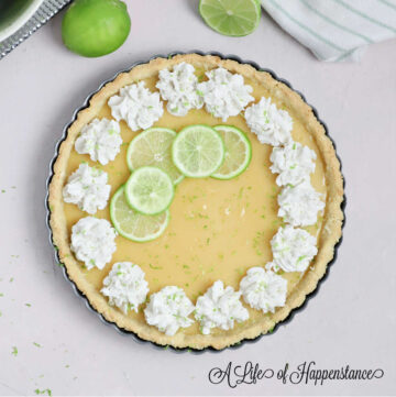 A coconut key lime pie on a pink table surrounded with limes.